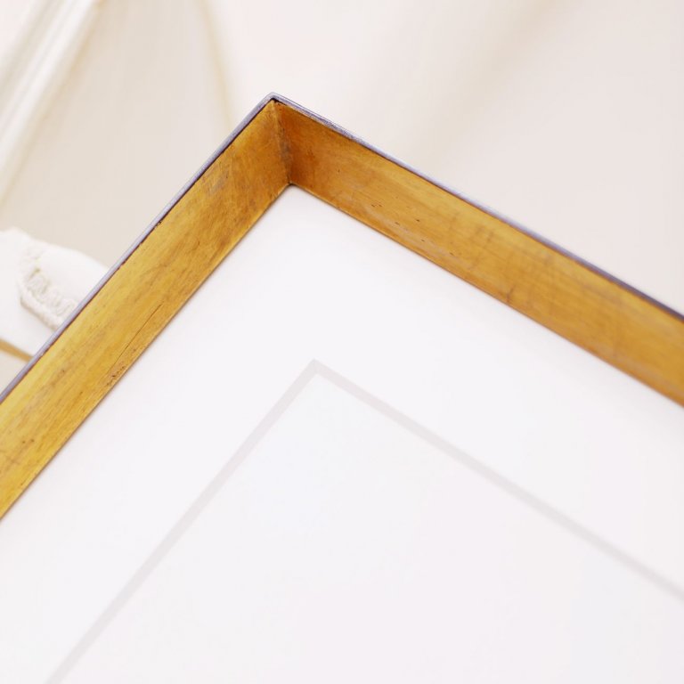 Zakázkový rám má tvar výrazně špičatého trojúhleníku, je vyzlacený plátkovým kovem, patinovaný a doplněný o hlubokou bílou paspartu, obraz Mrs Mia Wallace není téměř vidět. 