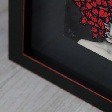 Detailní pohled na červené linky na hranách černého rámu s výsekem tisku Mariposas od Any Juan se kterým barevně dokonale ladí.