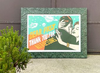 Neobvykle zarámovaný plakát od Pasty Onera s názvem Dear Past v moderním zeleném rámu s dekorem listů monstery bez použití pasparty. Tisk je umístěn v exteriéru a opřen o hnědá garážová vrata se zeleným keřem v popředí.