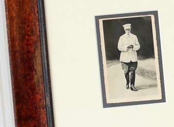Přiblížený pohled na historickou fotografii prezidenta Masaryka zarámovanou ve dvojici paspart s výsekem elegantního historizujícího dřevěného rámu s patinou.