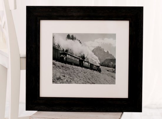 Novodobá reprodukce černobílé fotografie „Treno delle Dolomiti“ v širokém moderním dřevěném rámu z mořené borovice s bílou paspartou a antireflexním sklem se základním UV filtrem.