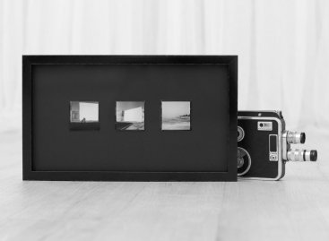 Tři malé čtvercové černobílé fotografie Kodak 400TMY od Olivera Kerverna zarámované v jediném moderním černém lesklém rámu s černou muzeální paspartou a muzeálním sklem. Vedle rámu je jako dekorace historická filmová kamera.