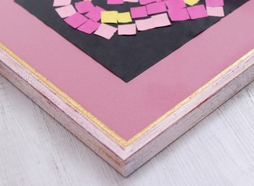 Dětská koláž ve tvaru srdce adjustovaná na původní podložce je položená na růžové paspartě, v přiblíženém pohledu je vidět, že se papír jemně vlní.