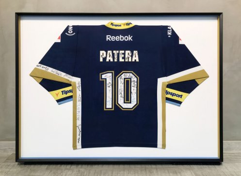 Detail rámování hokejového dresu Pavla Patery s vnitřními boky černého rámu v modrých a zlatých týmových barvách.