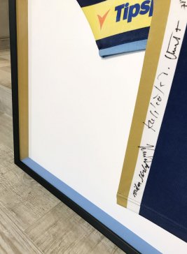Detail rámování hokejového dresu Pavla Patery s vnitřními boky černého rámu v modrých a zlatých týmových barvách.