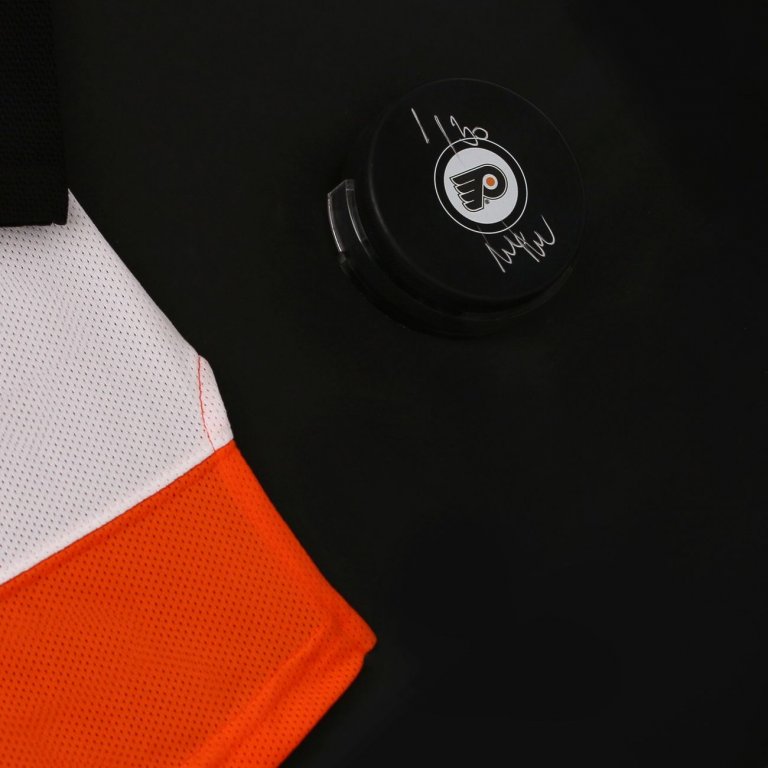 Podepsaný hokejový puk Philadelphia Flyers ve speciálním muzeálním držáku vložený jako doplněk do černého prostoru rámu se zarámovaným dresem Jakuba Voráčka.