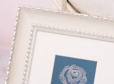 Detail paličkované krajky na modrém podkladu v toskánském smetanovém rámu se stříbrným ornamentem a paspartou.
