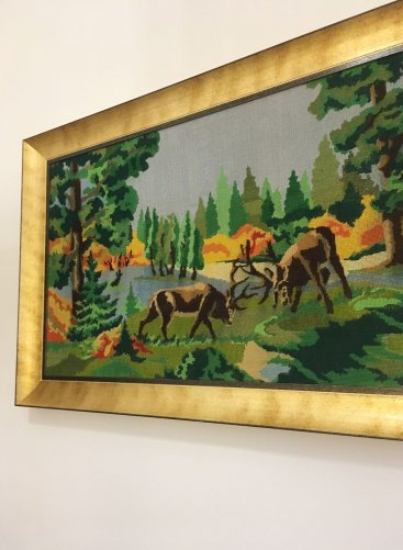 Stará výšivka se soby je napnutá na napínací podrám jako plátno