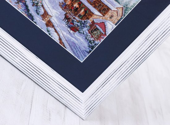 Zarámovaná výšivka Vánoční vesnice v bílo-modré kombinaci rámu a pasparty