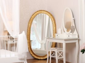 Neobvyklé luxusní oválné zrcadlo ve zlaceném moderně vyřezávaném rámu v interiéru dámské ložnice.