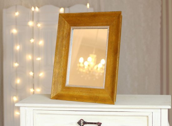 Žluté kosmetické zrcadlo na komodě obývacího pokoje, široký dřevěný rám s kartáčovanou strukturou a stříbrnou vnitřní linkou.