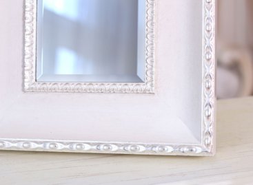 Široce broušená fazeta na zrcadle v širokém bílém dřevěném rámu s elegantní stříbrnou ozdobou perlovce a jemnou patinou.