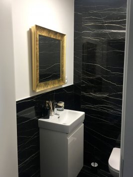 Designová koupelna v  moderním bytě v Praze 3 v černobílém provedení se čtvercovým zrcadlem s moderním lesklým zlaceným rámem a s broušenou fazetou.