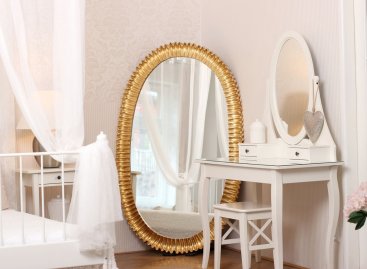 Neobvyklé luxusní oválné zrcadlo ve zlaceném moderně vyřezávaném rámu v interiéru dámské ložnice