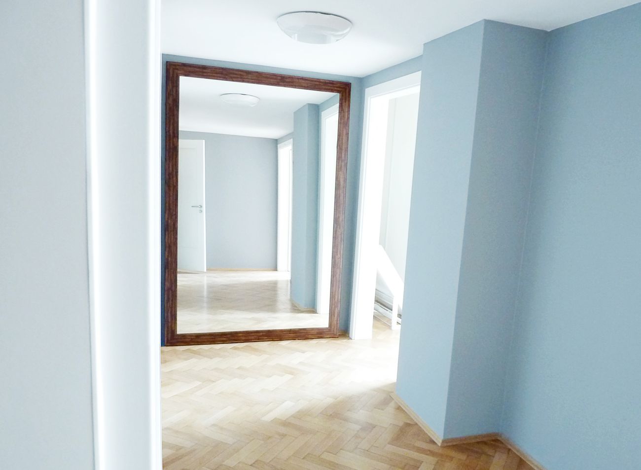 Velké XXL zrcadlo v dřevěném rámu opřené o zeď v interiéru moderní kanceláře | © Frameit