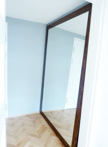 Velké XXL zrcadlo v dřevěném rámu opřené o zeď v interiéru moderní kanceláře